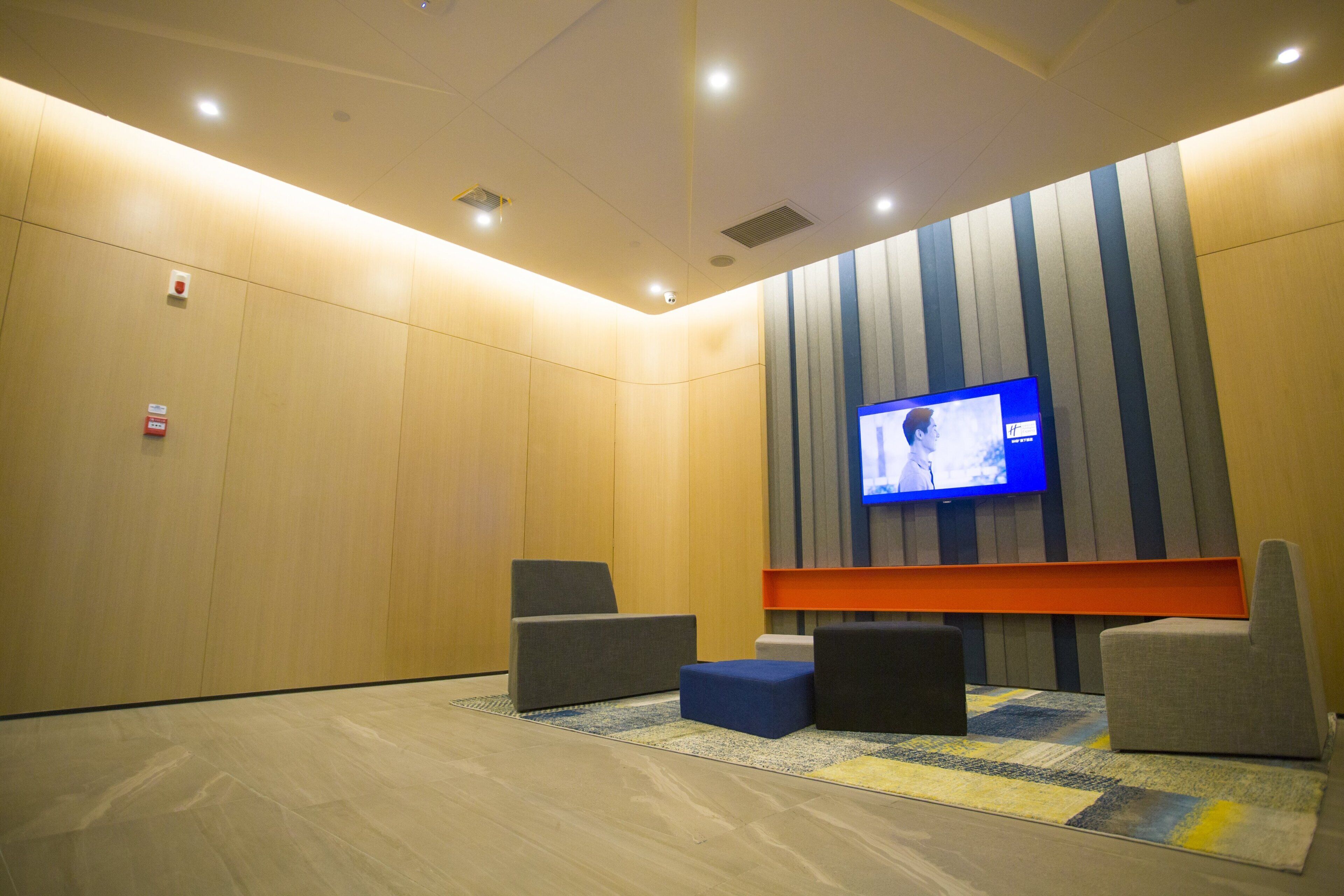 Un área de espera moderna con una televisión de pantalla plana en la pared, asientos acolchados y una alfombra estampada.