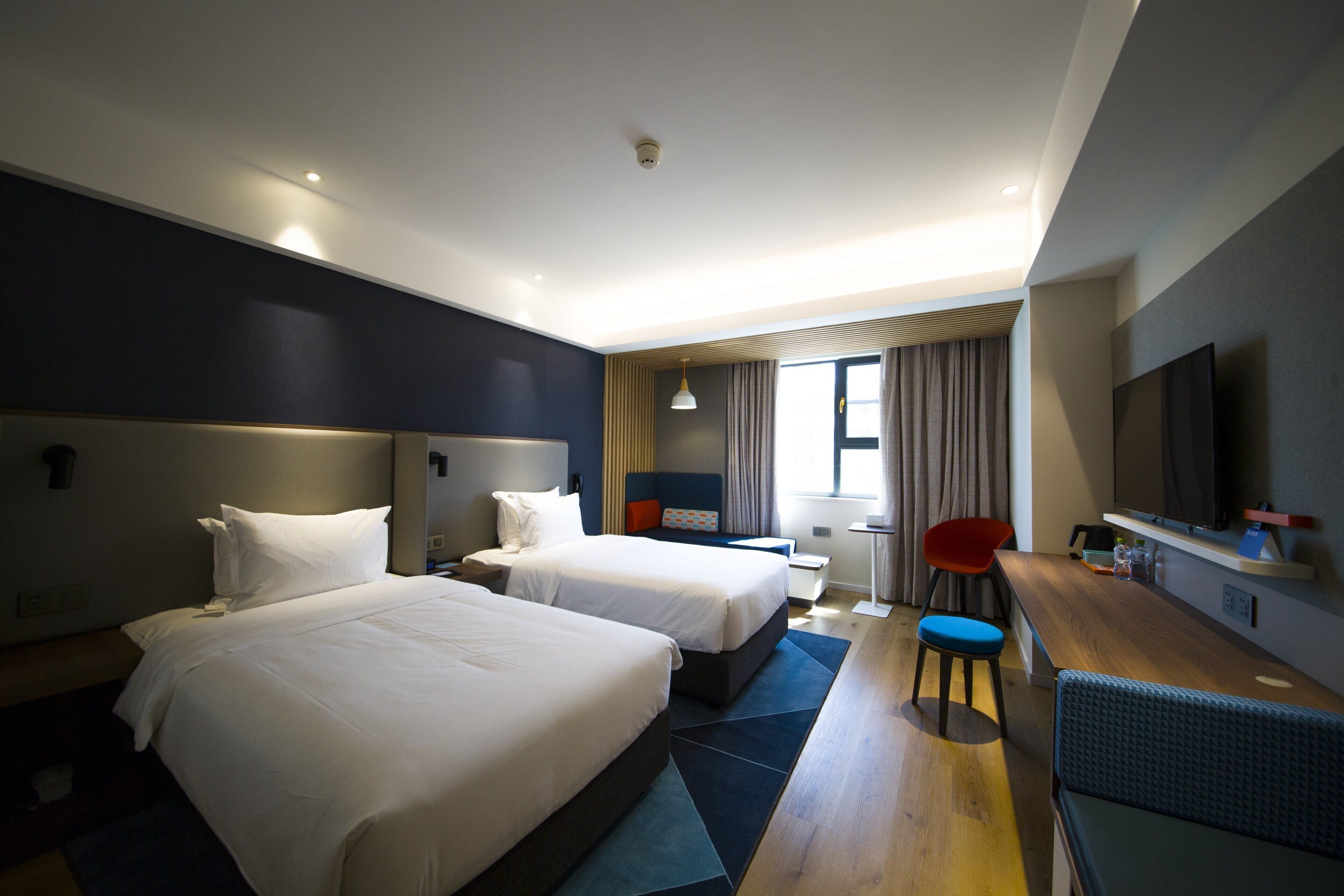 Une chambre d’hôtel avec deux lits, un bureau, une chaise, une télévision et une fenêtre avec des rideaux.