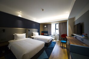 Une chambre d’hôtel avec deux lits, un bureau, une chaise, une télévision et une fenêtre avec des rideaux.