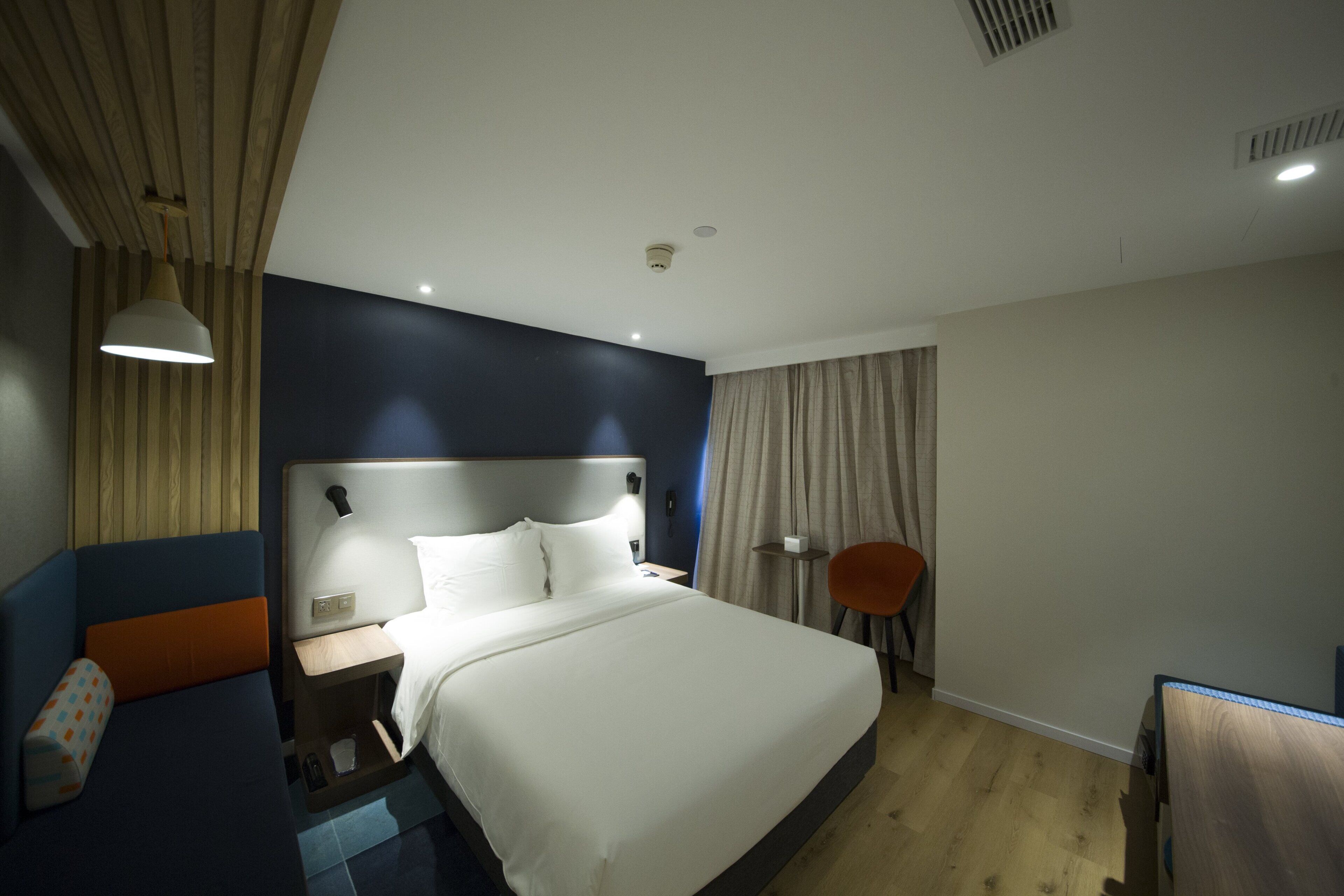 Habitación de hotel moderna con una cama grande, mesita de noche, lámpara y una silla.