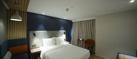Habitación de hotel moderna con una cama grande, mesita de noche, lámpara y una silla.