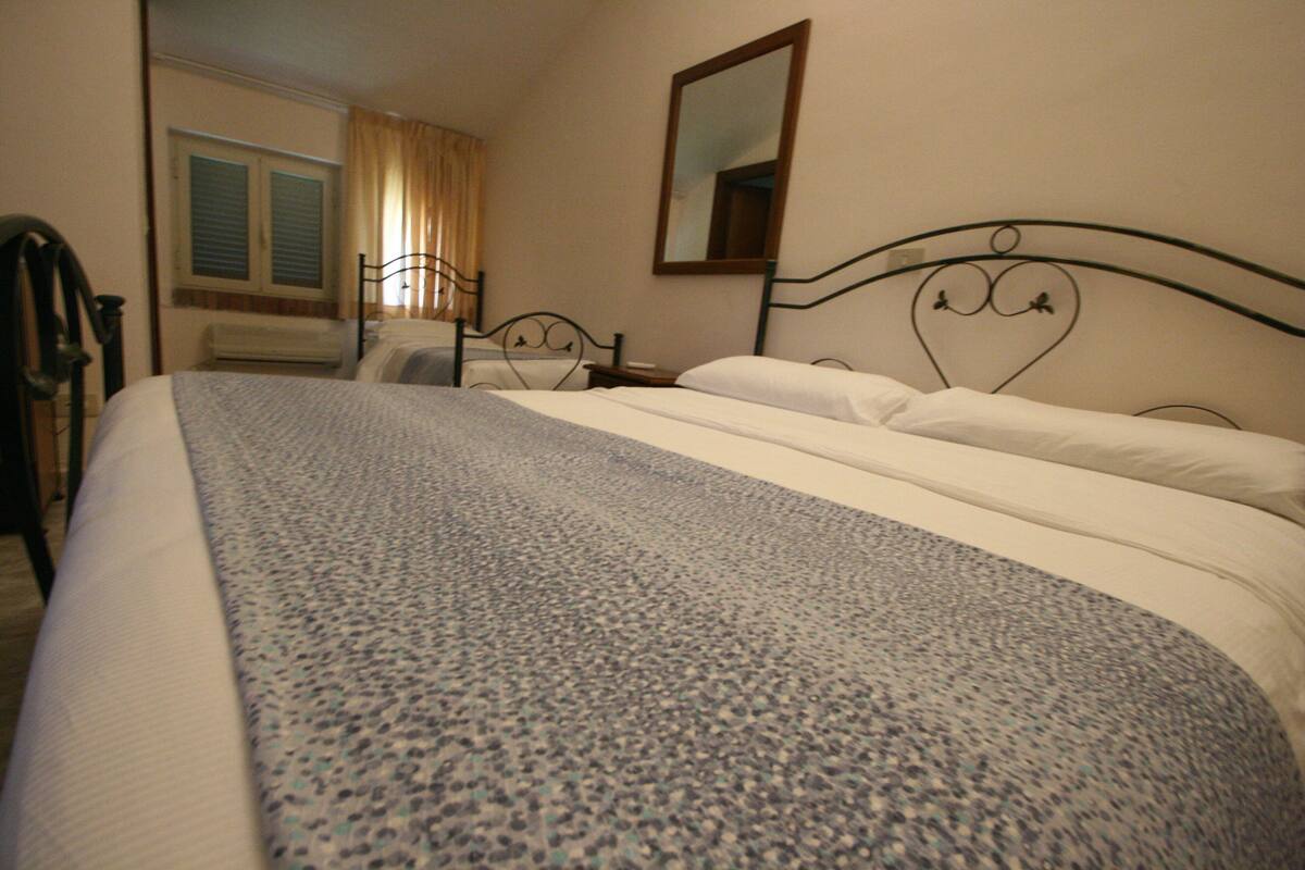 Una habitación de hotel con cama, una ventana con cortinas, un aire acondicionado y un espejo en la pared.