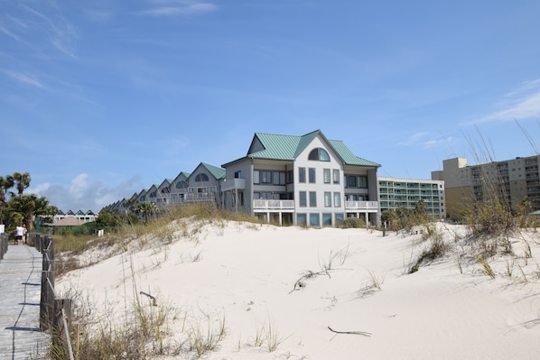 A beachfront hotel with multiple buildings, a sandy beach, and a wooden boardwalk. - Paradise is calling 🌴 Pick up! The beach is more affordable than you think! (Gulf Shores)