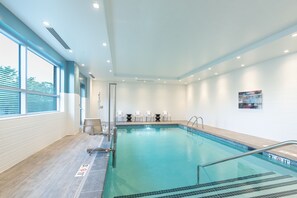 An indoor swimming pool with clear water, a diving board, and a set of chairs near the pool. - Holiday Inn Boston Logan Airport - Chelsea by IHG (Chelsea)
