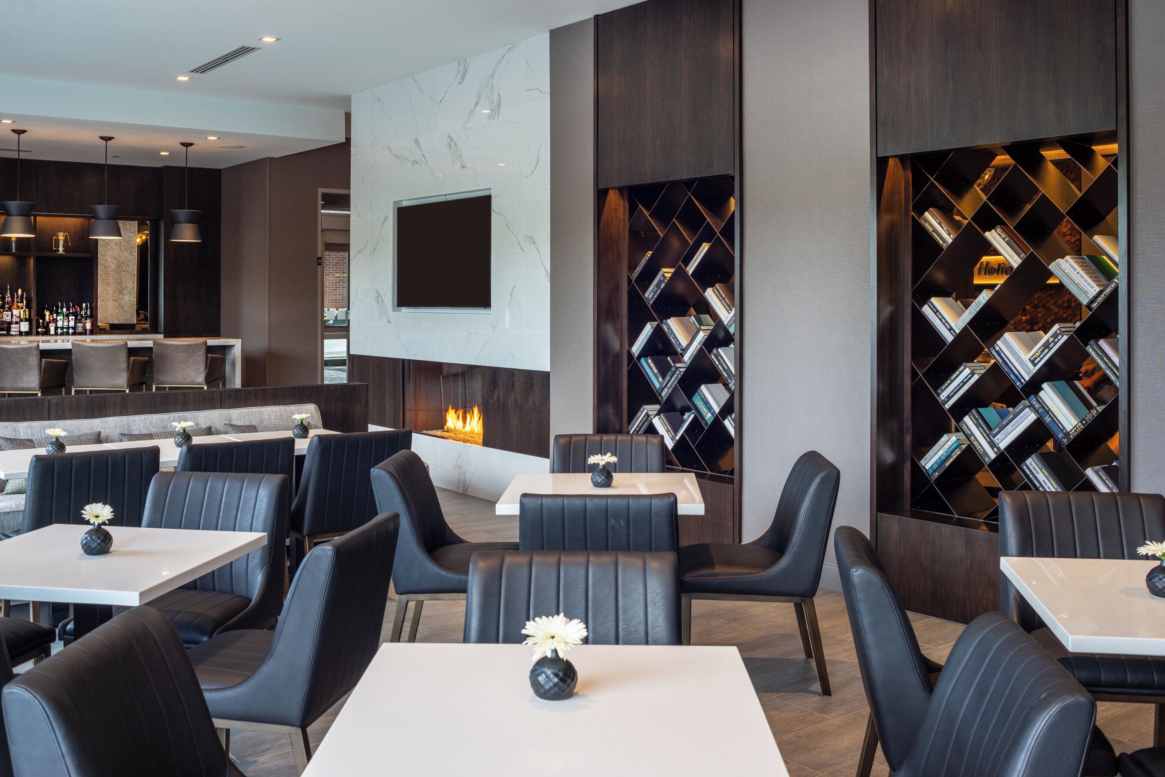 Interior moderno de restaurante con sillas de cuero negro, mesas blancas, una zona de bar y una chimenea.