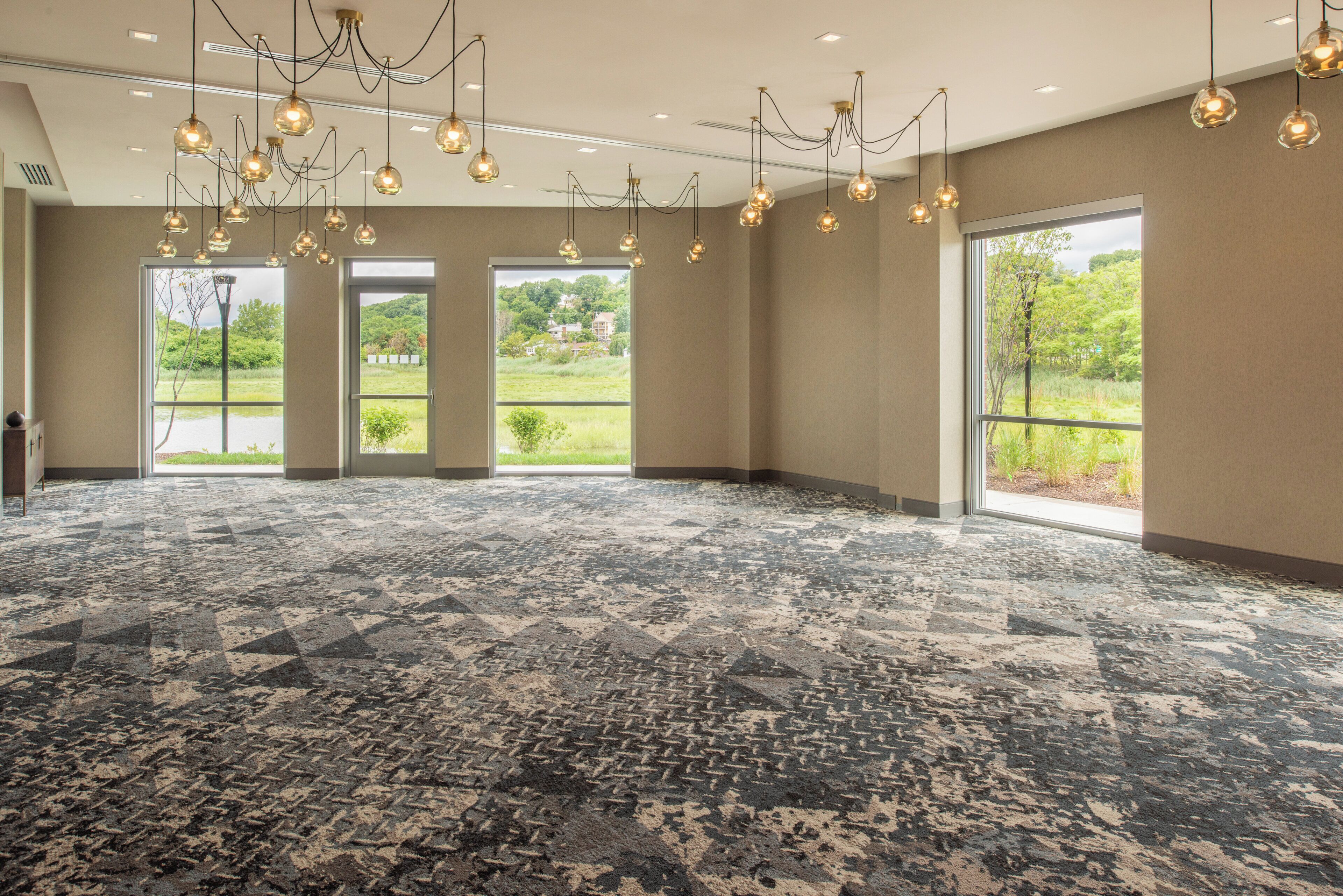 A spacious room with a patterned carpet, large windows, and hanging pendant lights.