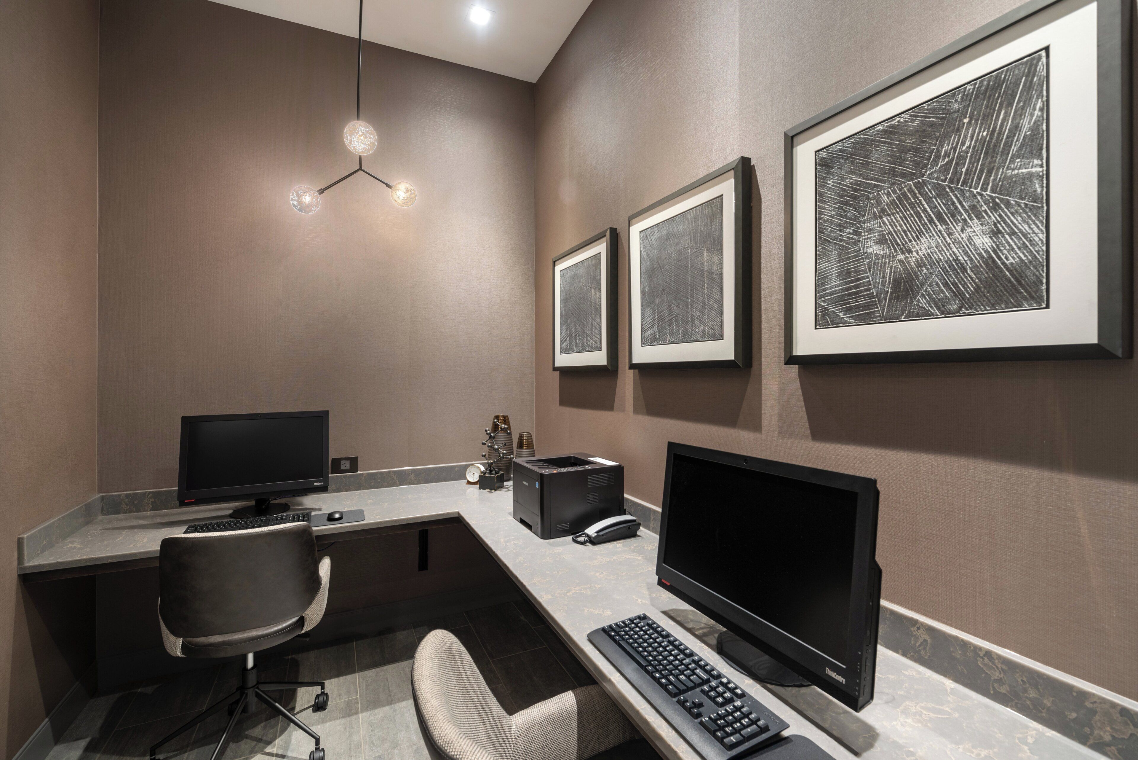 A modern office space with a desk, two monitors, a keyboard, a chair, and framed artwork on the wall.