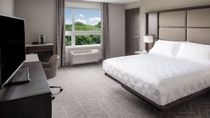 A hotel room with a large bed, a desk with a flat-screen TV, a chair, and a window with a view of greenery. - Holiday Inn Boston Logan Airport - Chelsea by IHG (Chelsea)