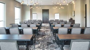 Un salón de conferencias con filas de mesas y sillas, una alfombra estampada e iluminación colgante.