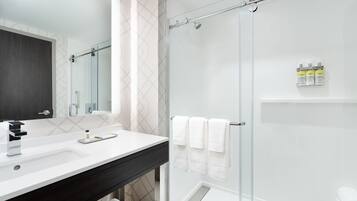 A modern bathroom with a glass shower enclosure, a white sink with a dark countertop, and a mirror above the sink.