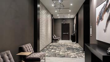 A modern hotel lobby with a seating area, a reception desk, and a patterned carpet.
