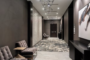A modern hotel lobby with a seating area, a reception desk, and a patterned carpet.