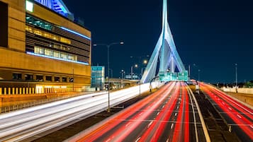 A modern bridge with light trails from moving vehicles, a large building with illuminated windows, and a clear night sky.