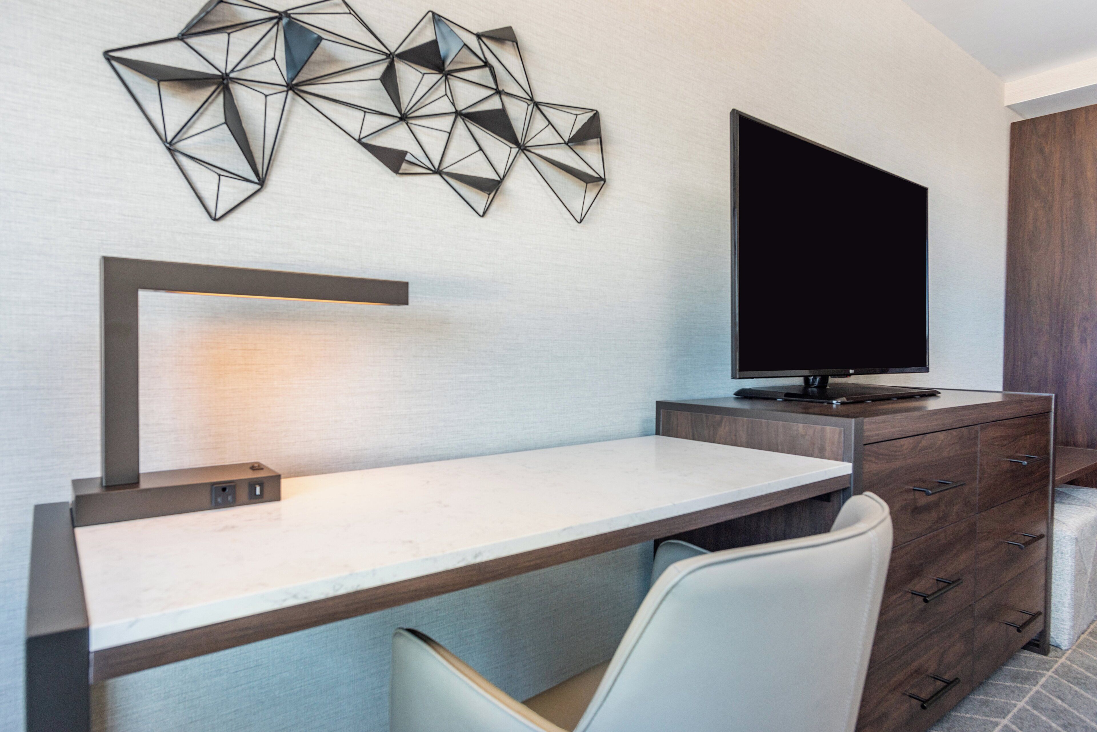 Une chambre d’hôtel moderne équipée d’un bureau, d’un téléviseur à écran plat et d’un élément décoratif mural.