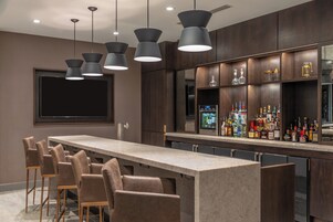 A bar area with a long counter, multiple bar stools, and a variety of liquor bottles.