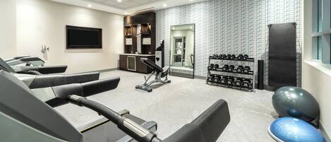 Un gimnasio con equipo de ejercicio, un espejo y una televisión montada en la pared.