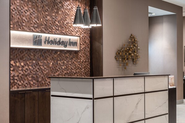 A reception desk with a sign reading "Holiday Inn" and a decorative wall with a geometric pattern. - Holiday Inn Boston Logan Airport - Chelsea by IHG (Chelsea)