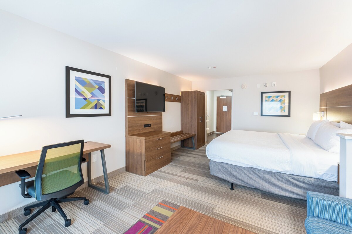 A hotel room with a bed, desk, chair, wardrobe, and artwork on the walls.