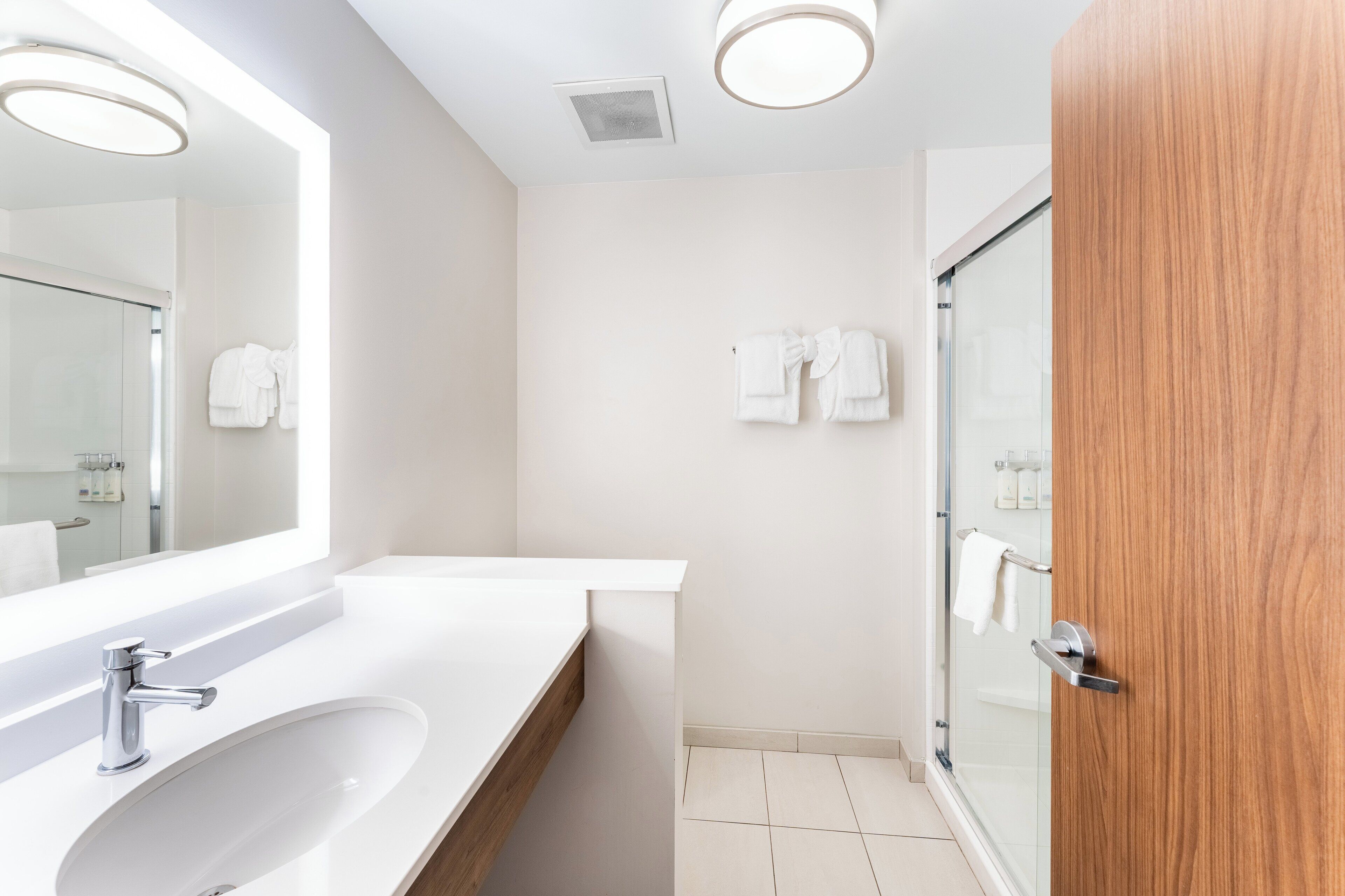 A modern bathroom with a white sink, mirror, and glass shower door.