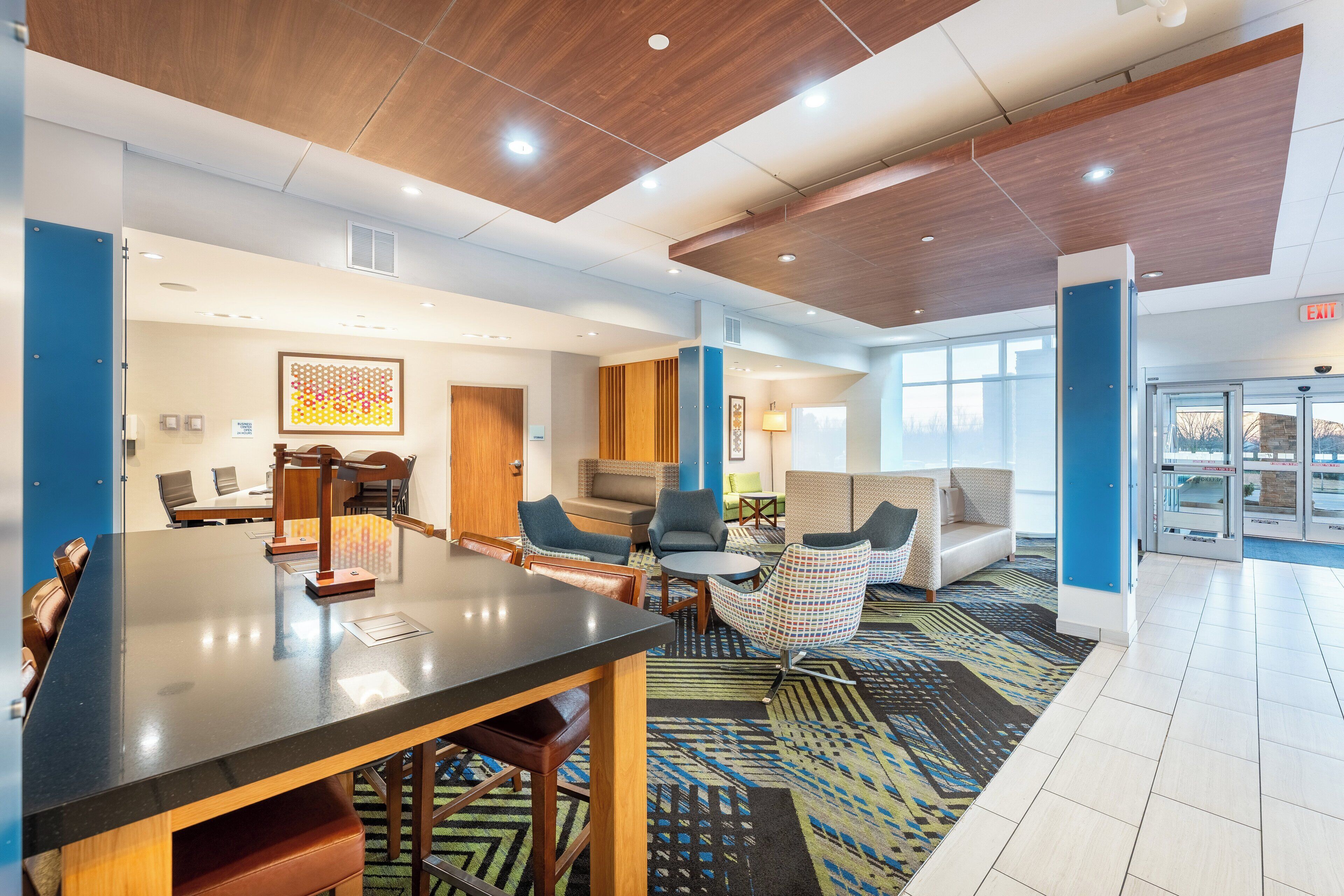 A modern hotel lobby with a long reception desk, comfortable seating areas, and a patterned carpet.