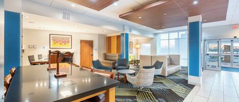 A modern hotel lobby with a long reception desk, comfortable seating areas, and a patterned carpet.