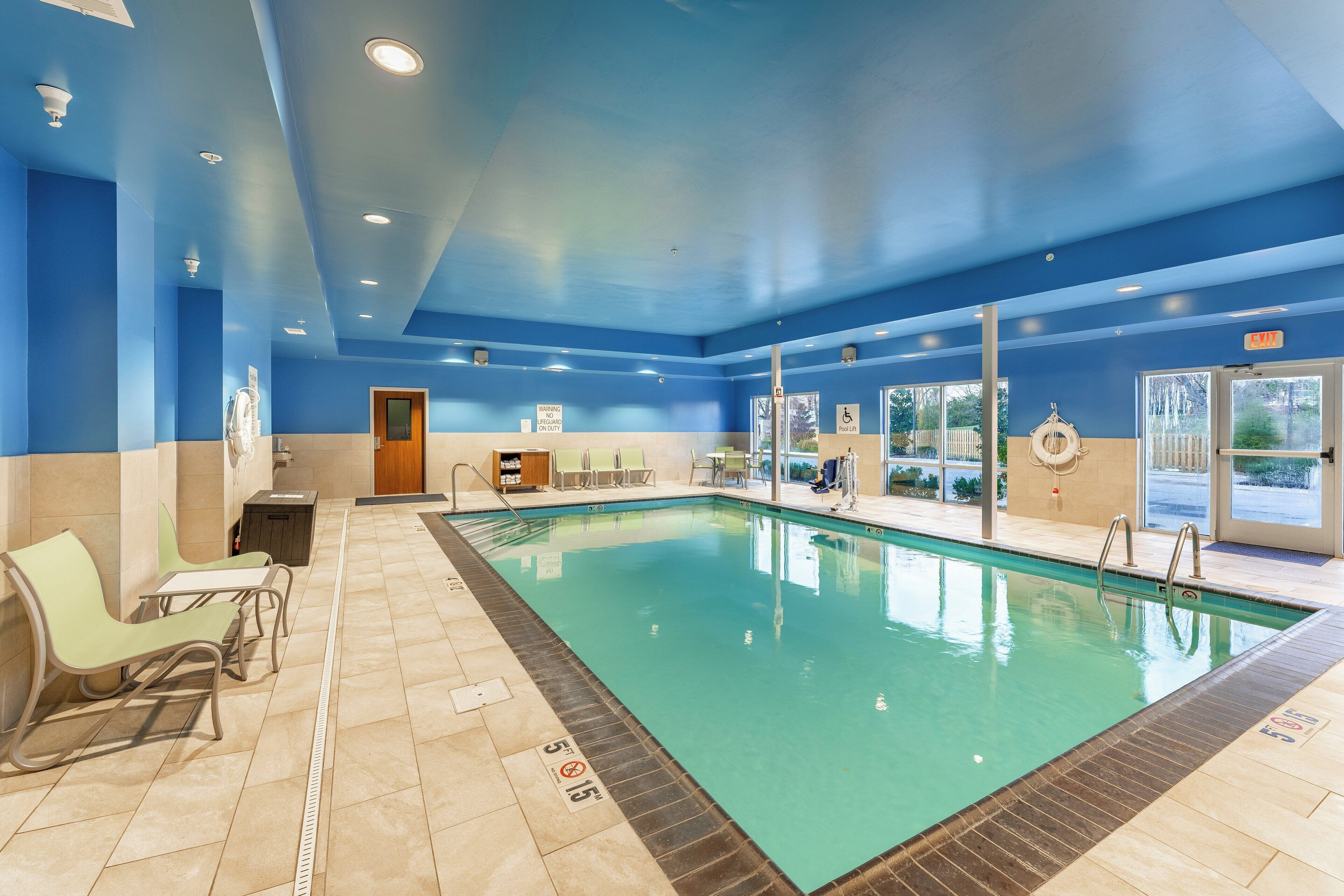 An indoor swimming pool with clear lane markings, a lifeguard chair, and a changing room area.