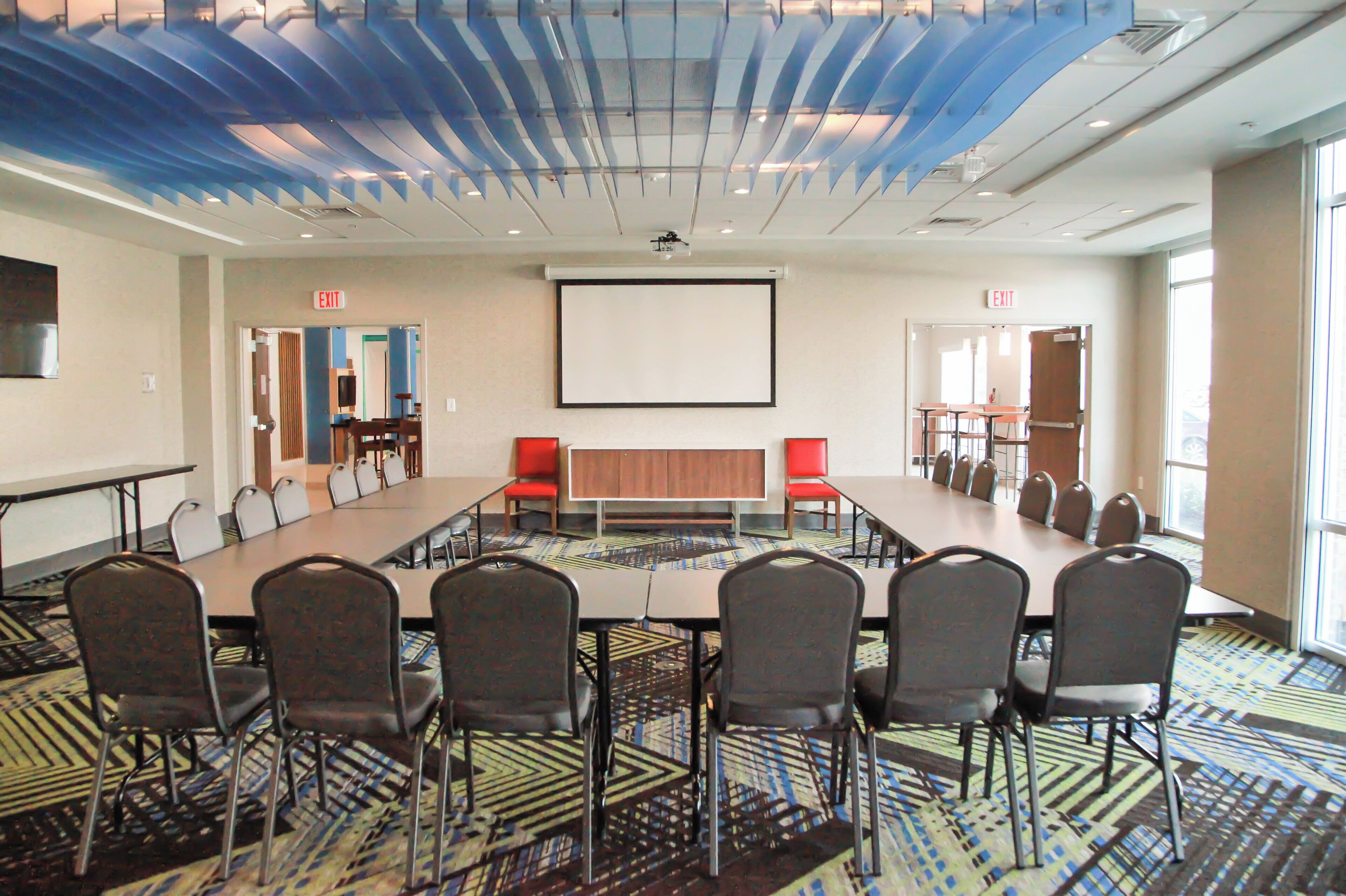 Un salón de conferencias con una larga mesa, varias sillas y una pantalla para proyector.