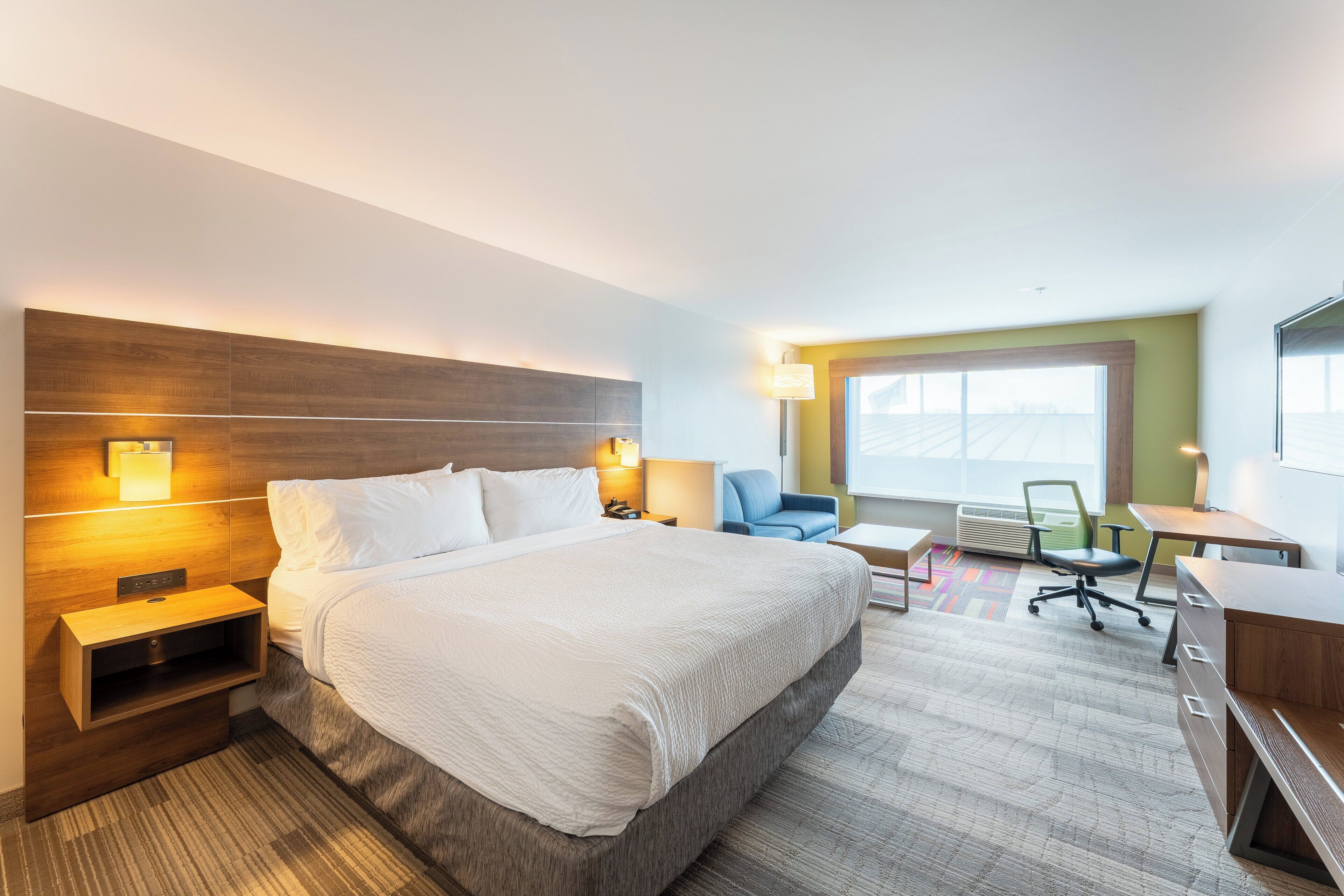 A hotel room with a large bed, bedside tables, a desk, a chair, and a window with a view.