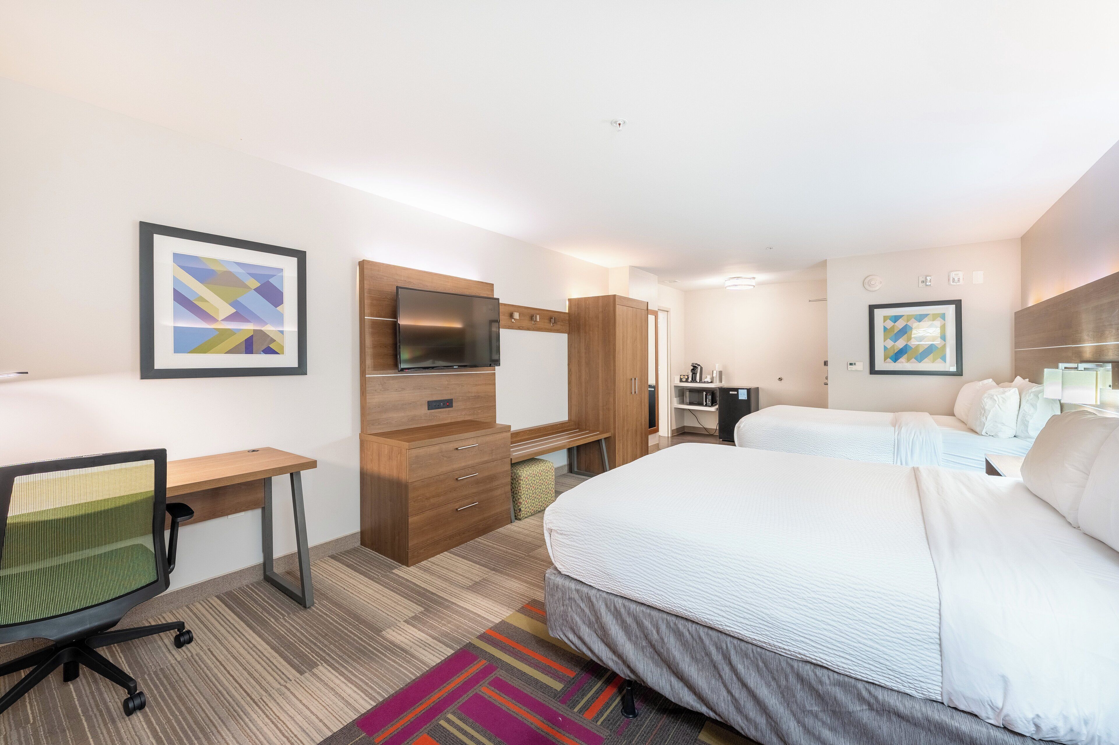A hotel room with a bed, desk, chair, TV, and artwork on the walls.