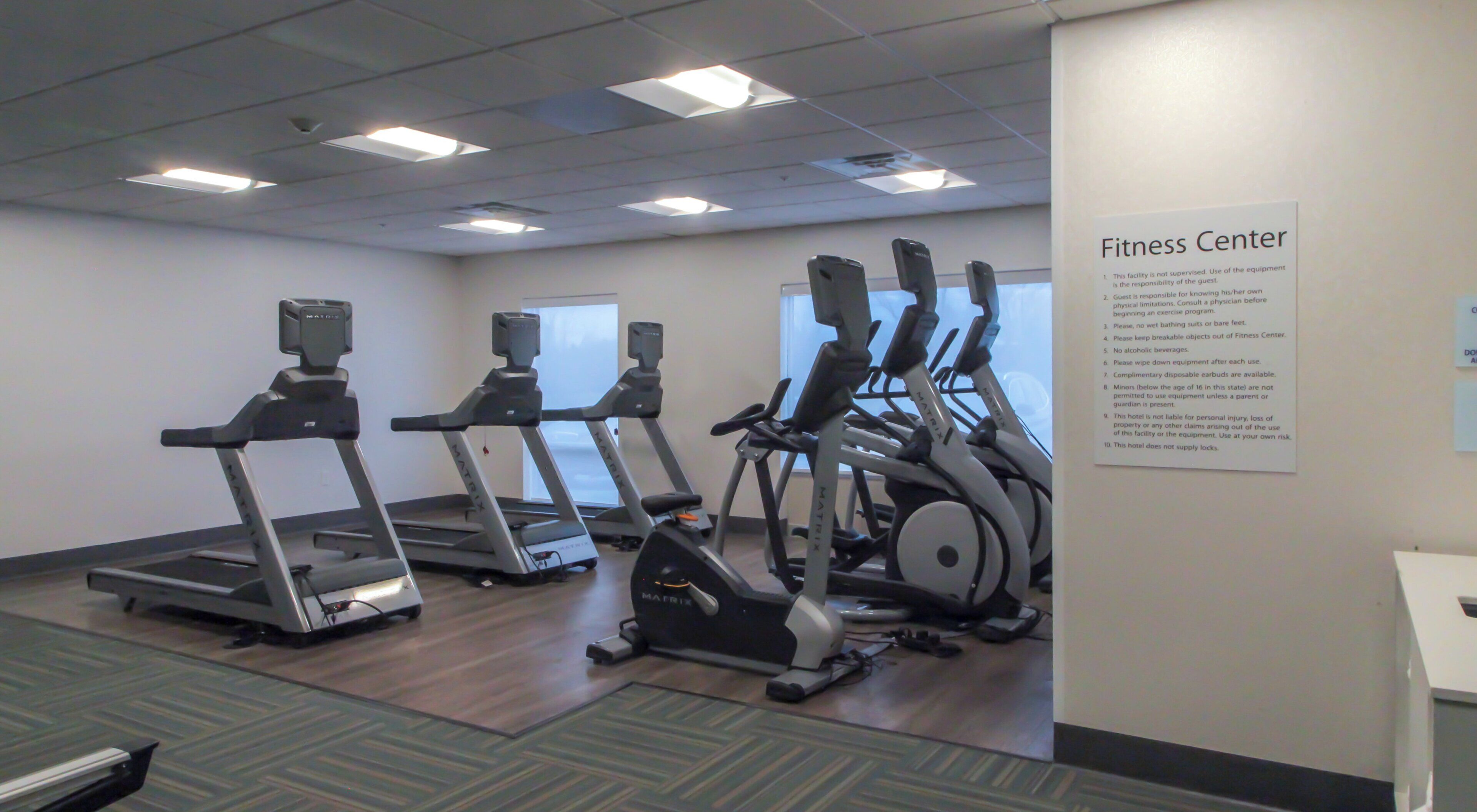A fitness center with treadmills, elliptical machines, and a wall sign with rules.