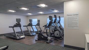 A fitness center with treadmills, elliptical machines, and a wall sign with rules.