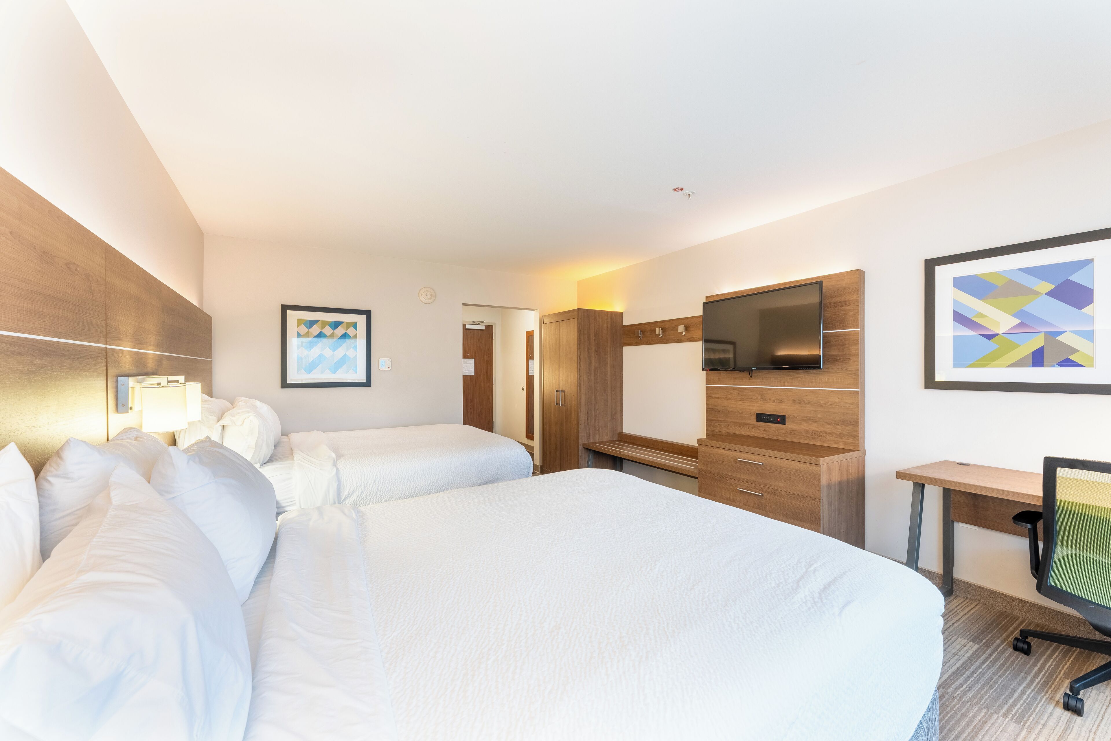 Habitación de hotel con dos camas, un escritorio, televisor y un cuadro en la pared.