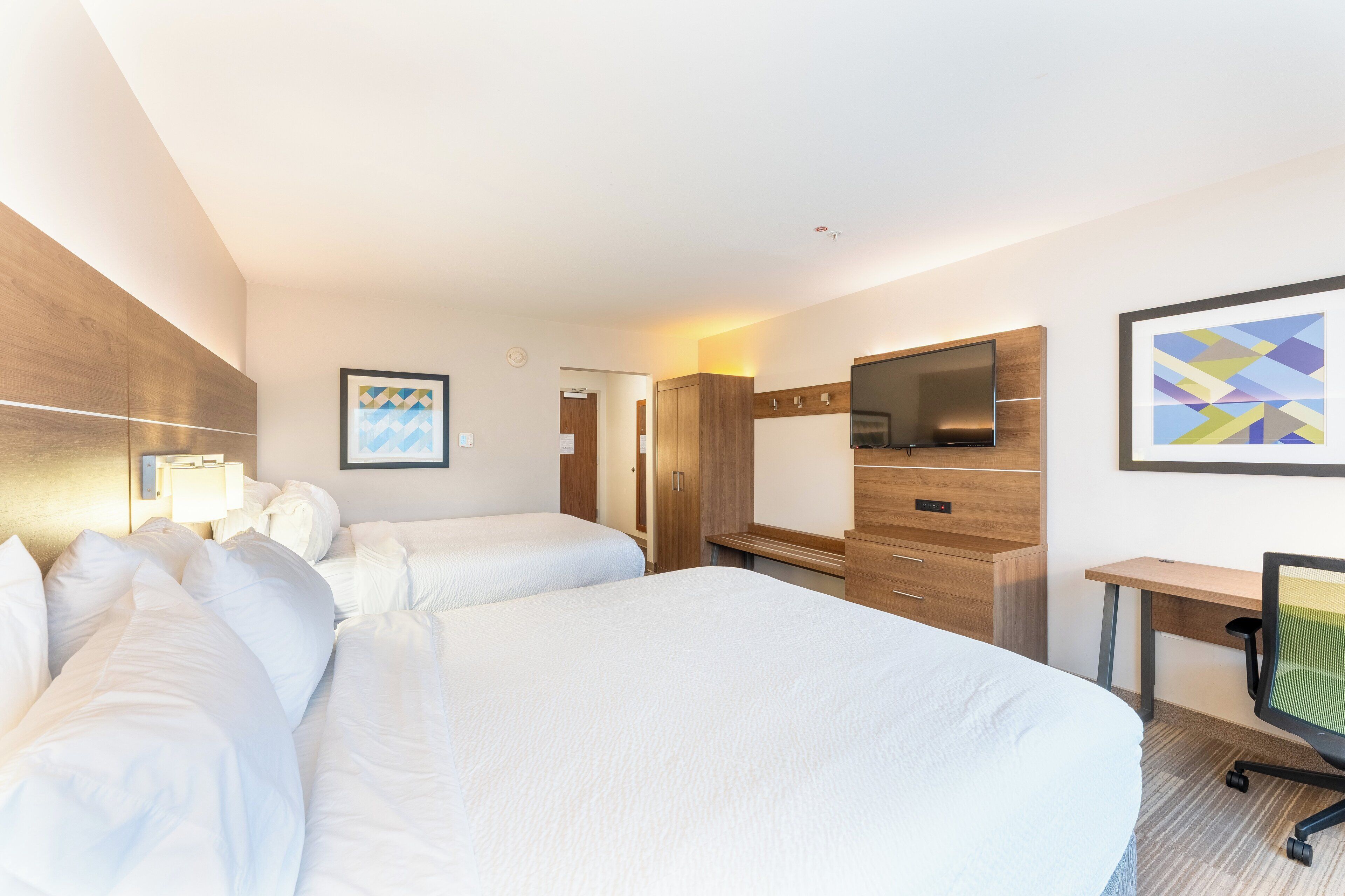 Habitación de hotel con dos camas, un escritorio, un televisor y un cuadro en la pared.