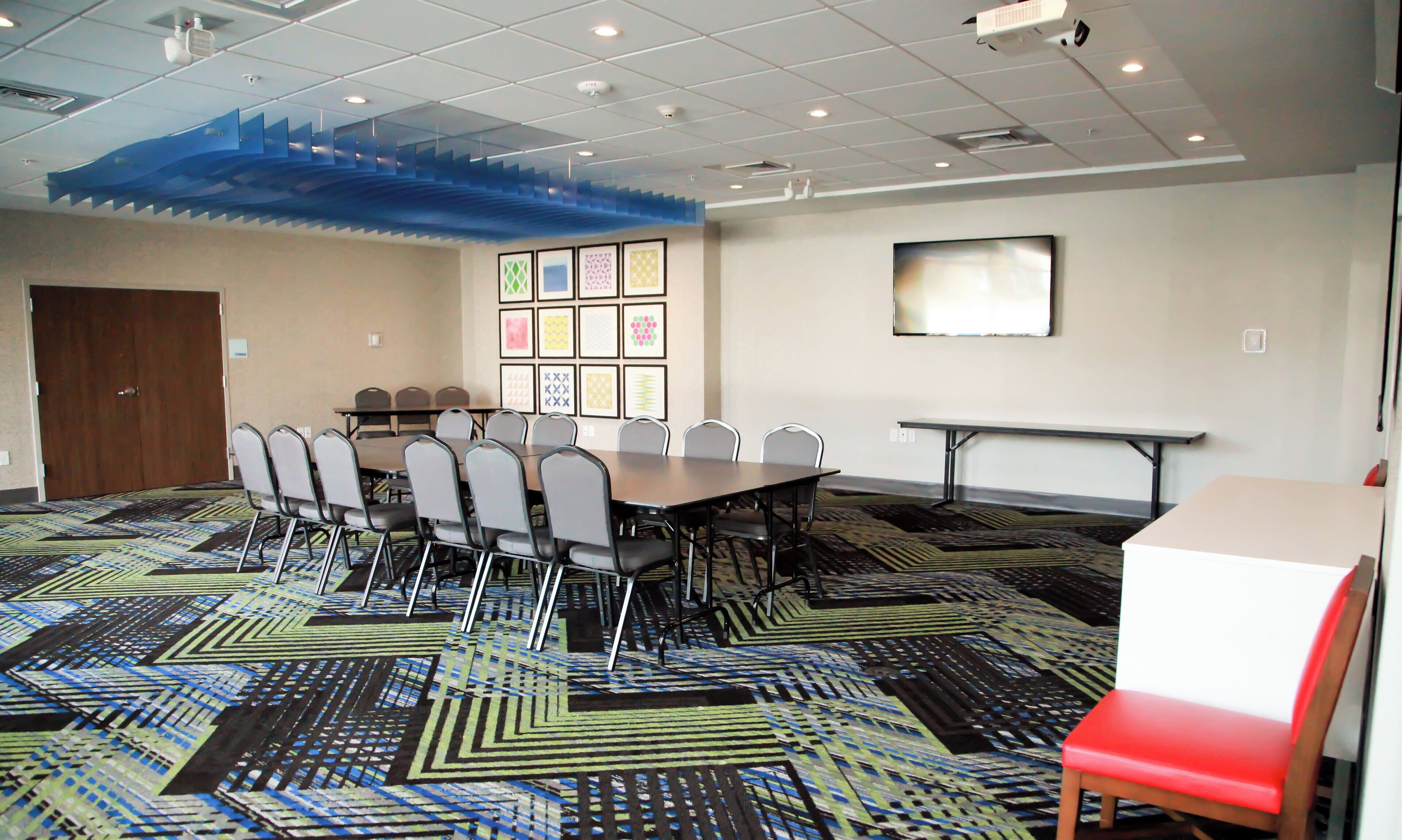 A conference room with a long table, chairs, a projector screen, and patterned carpet.