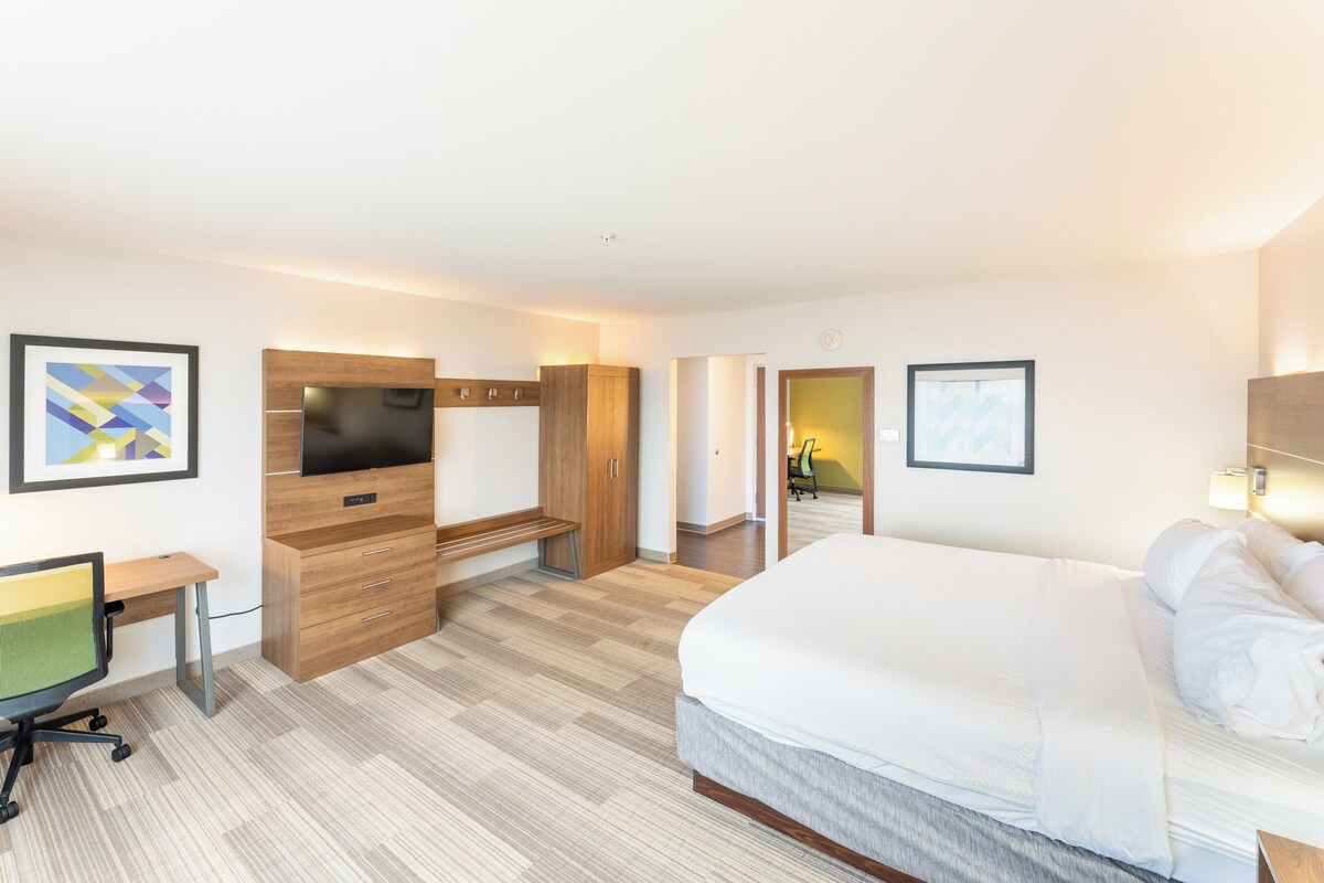 A modern hotel room with a large bed, a desk with a computer, a TV, and a wardrobe.