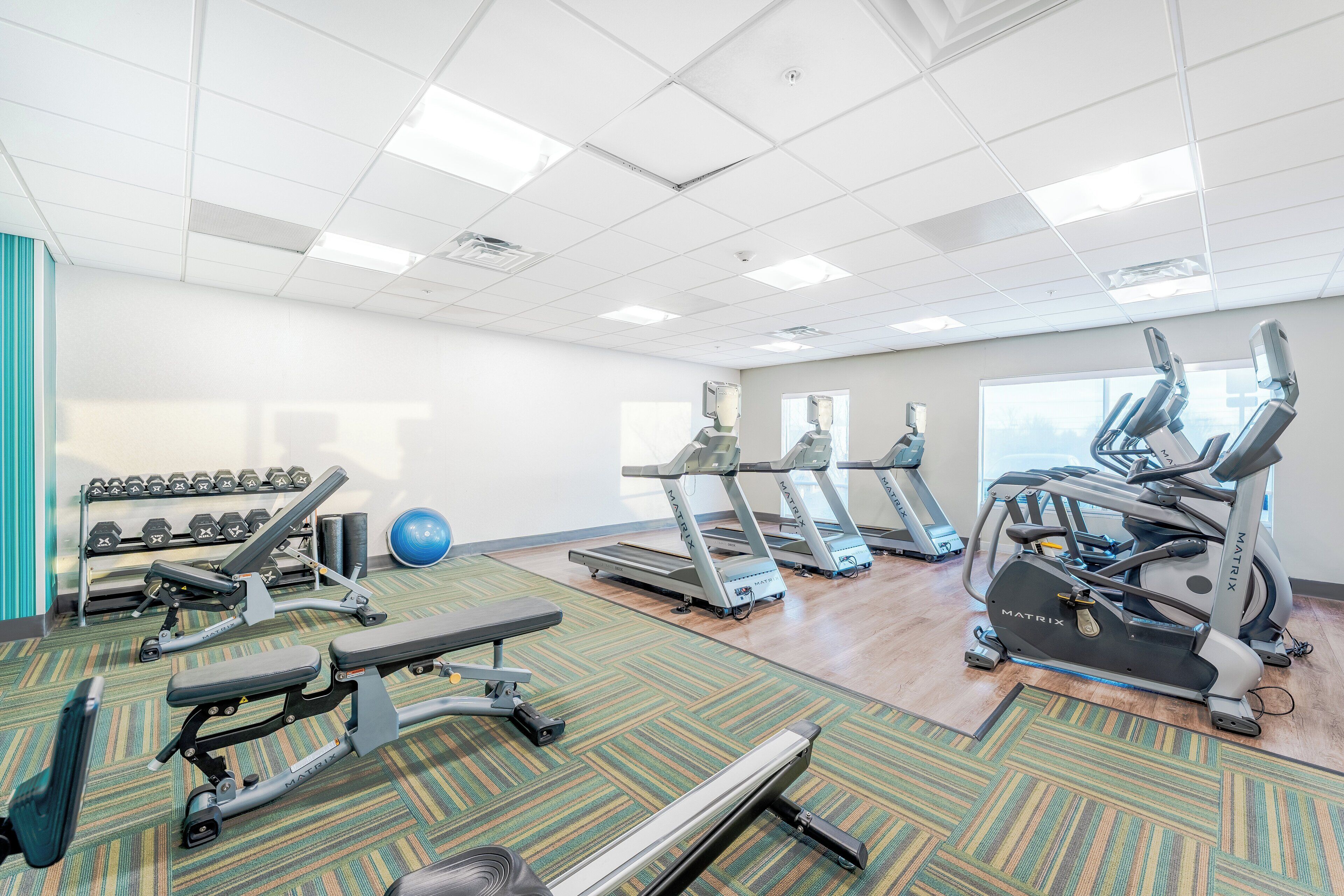 A gym with treadmills, elliptical machines, dumbbells, and exercise balls.