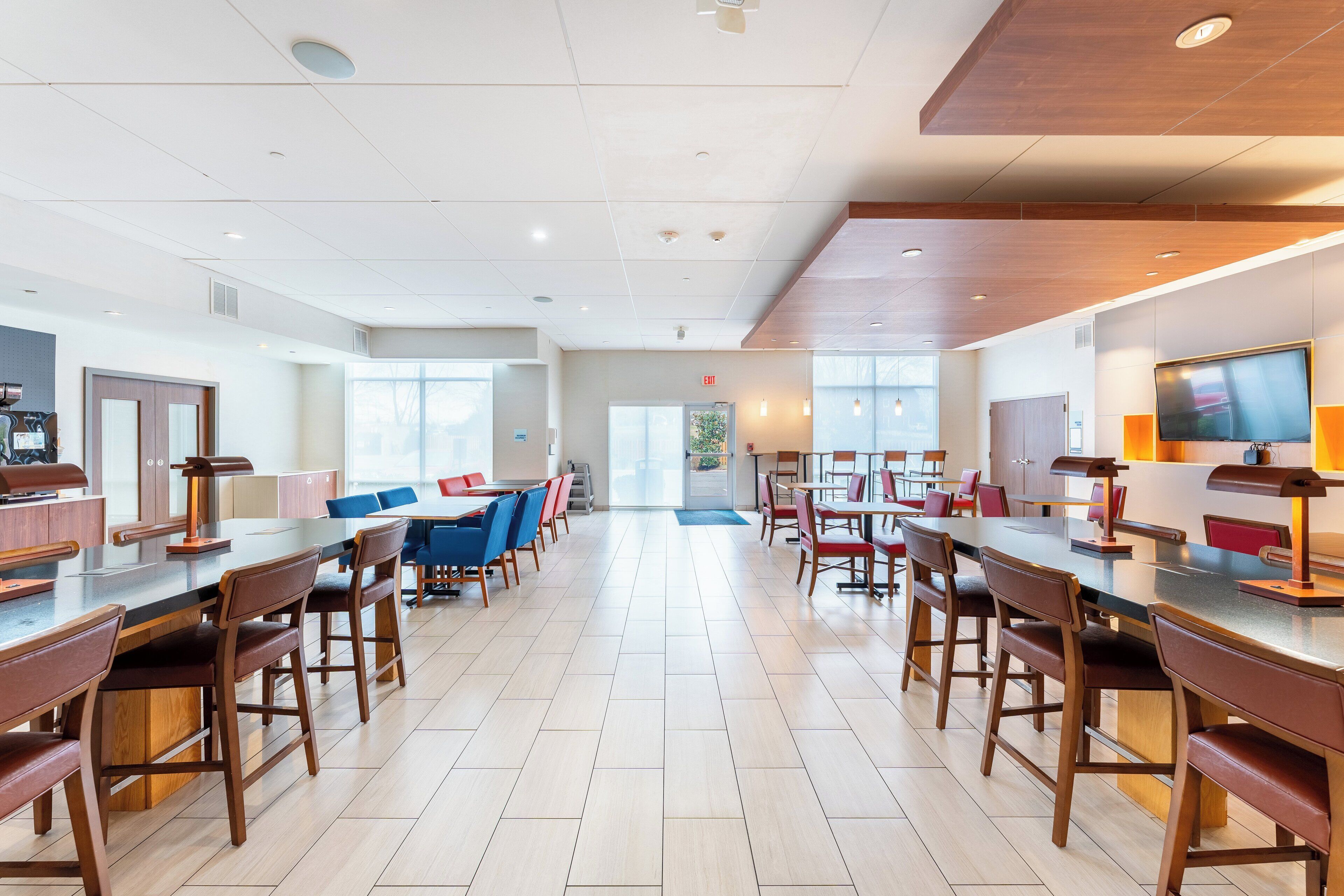 Een ruime hotel lobby met meerdere zithoeken, een groot televisiescherm en een helder uitzicht op het buitenlands landschap door de ramen.