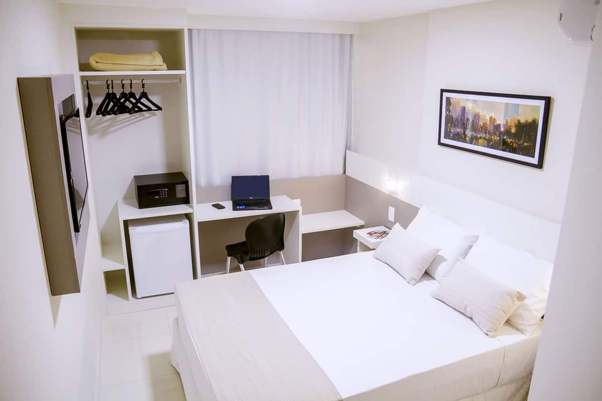 Een hotelkamer met een bed, een bureau, een stoel, een kledingkast en een stadsgezicht schilderij.