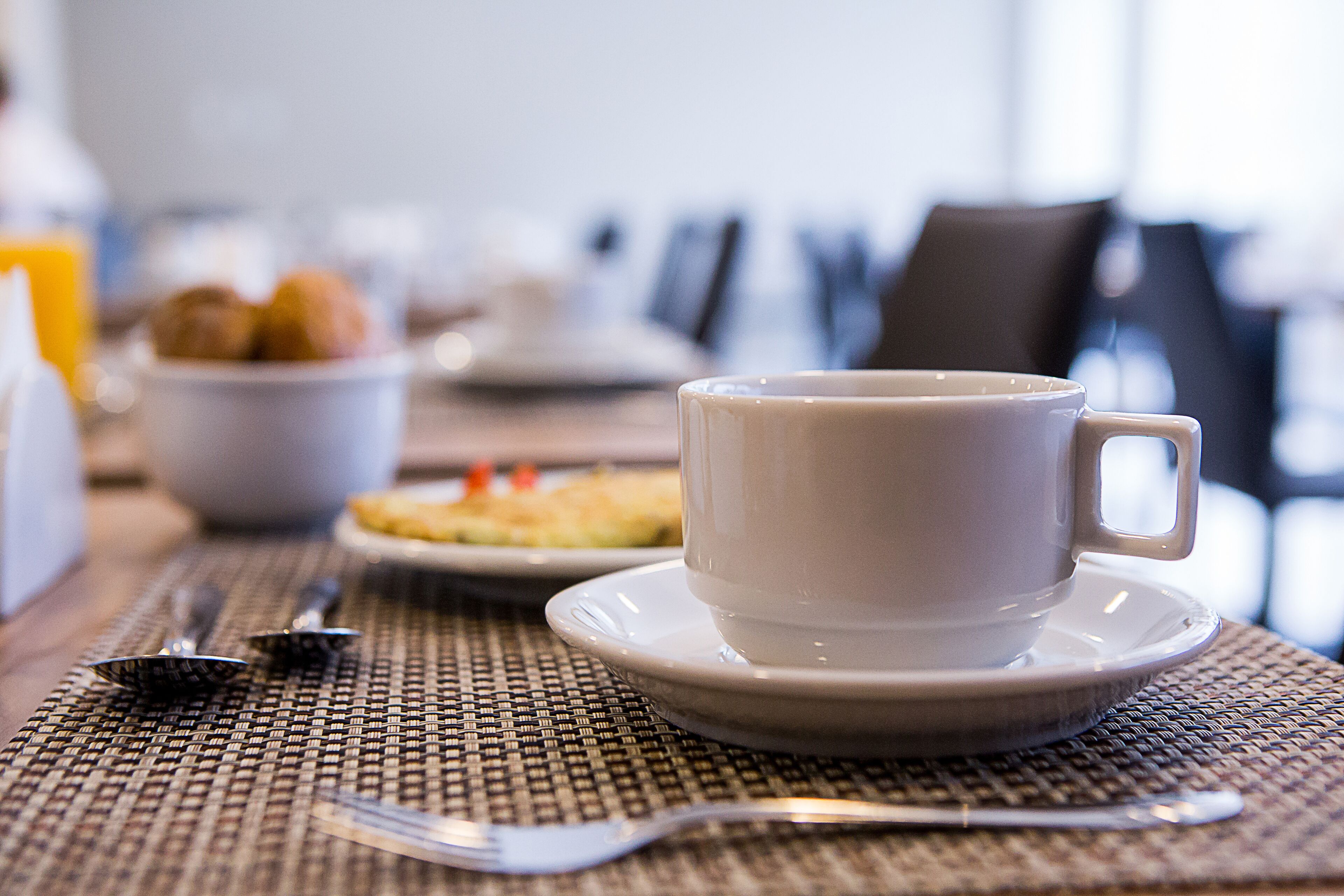 A breakfast setting with a cup, plate, and utensils on a woven table mat.