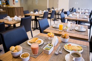 A breakfast setting with tables set for dining, including plates of toast, a bowl of fruit, a smoothie, and a cup of coffee. - Trip Hotel Ubá (Uba)