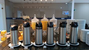 Un bufé de desayuno con varios dispensadores de bebidas etiquetados para agua, leche y jugo.