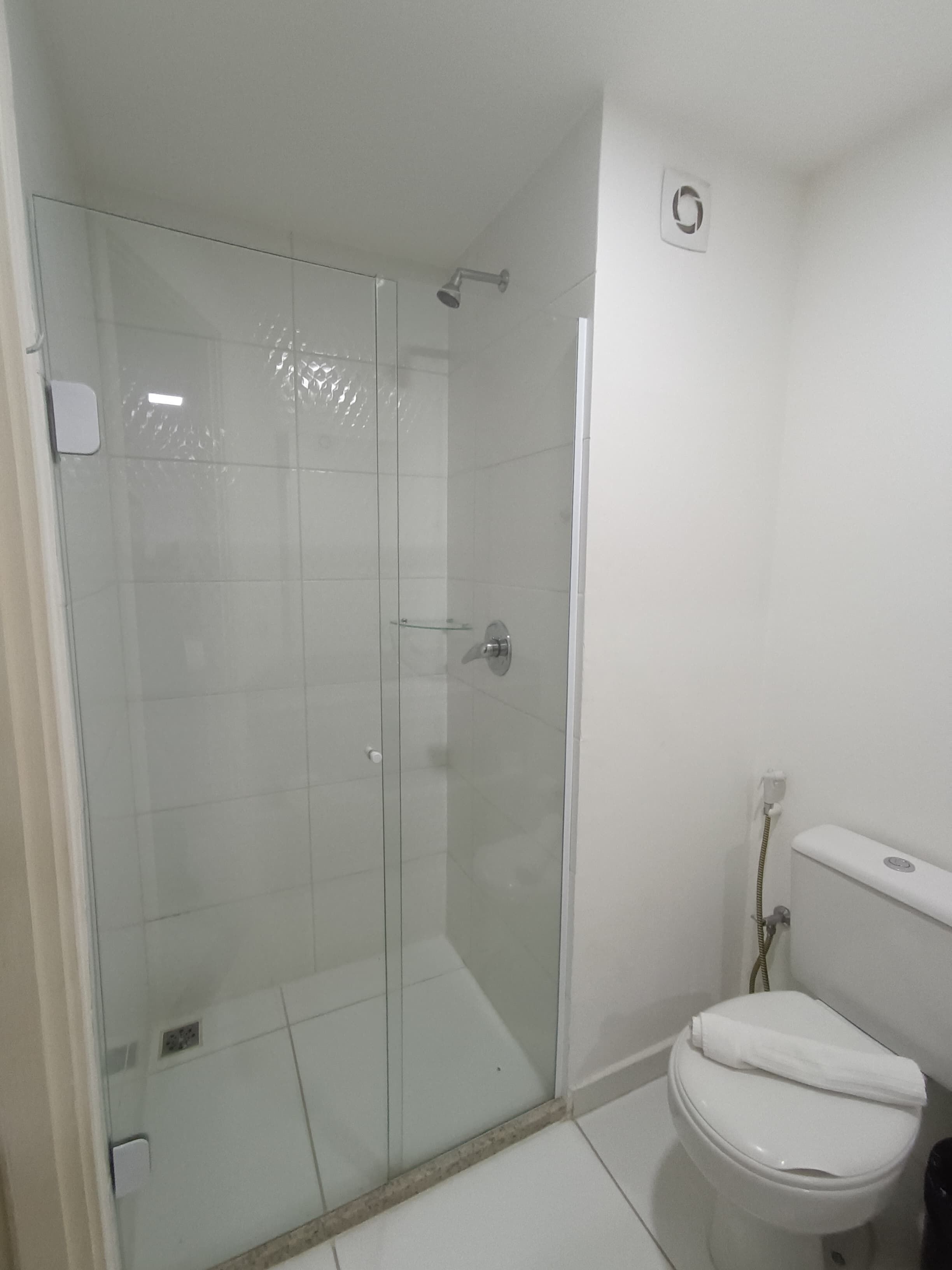 Un baño con ducha de mampara de vidrio, un inodoro blanco y un enchufe a la vista en la pared.