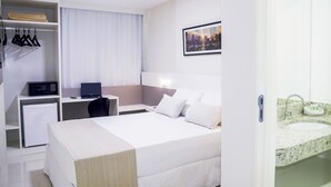 A hotel room with a bed, a desk with a laptop, a small refrigerator, a wardrobe, and a bathroom with a sink and mirror. - Trip Hotel Ubá (Uba)