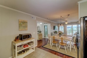 Un coin repas avec une table et des chaises en bois, un four à micro-ondes posé sur un meuble blanc et un réfrigérateur.