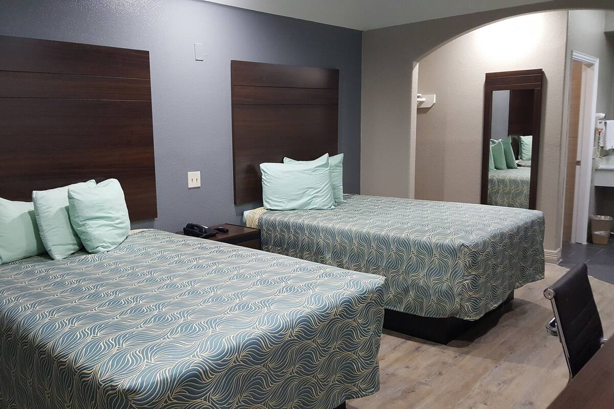 A hotel room with two beds, each with patterned bedding, a dark headboard, and a nightstand with a phone.