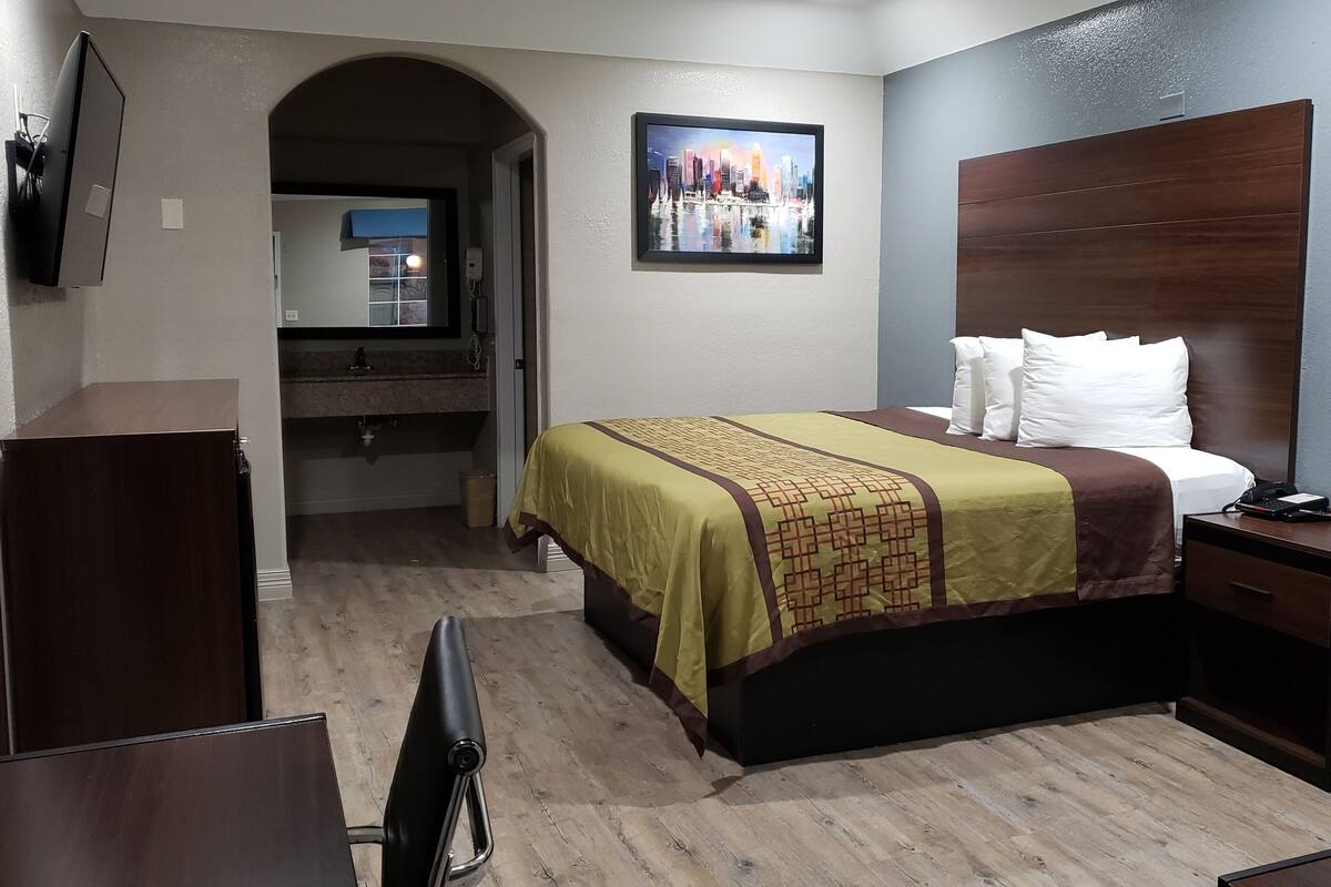 A hotel room with a bed, a desk, a TV, a bathroom, and a cityscape painting on the wall.