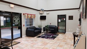 A lobby with a reception desk, two black leather sofas, a potted plant, a television, and a sign indicating the address of the hotel. - Palace Inn Hwy 6 North & Clay Rd (Houston)