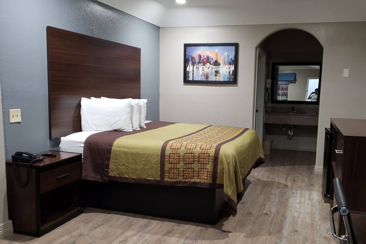 A hotel room with a bed, a desk, a phone, a mirror, and a TV.