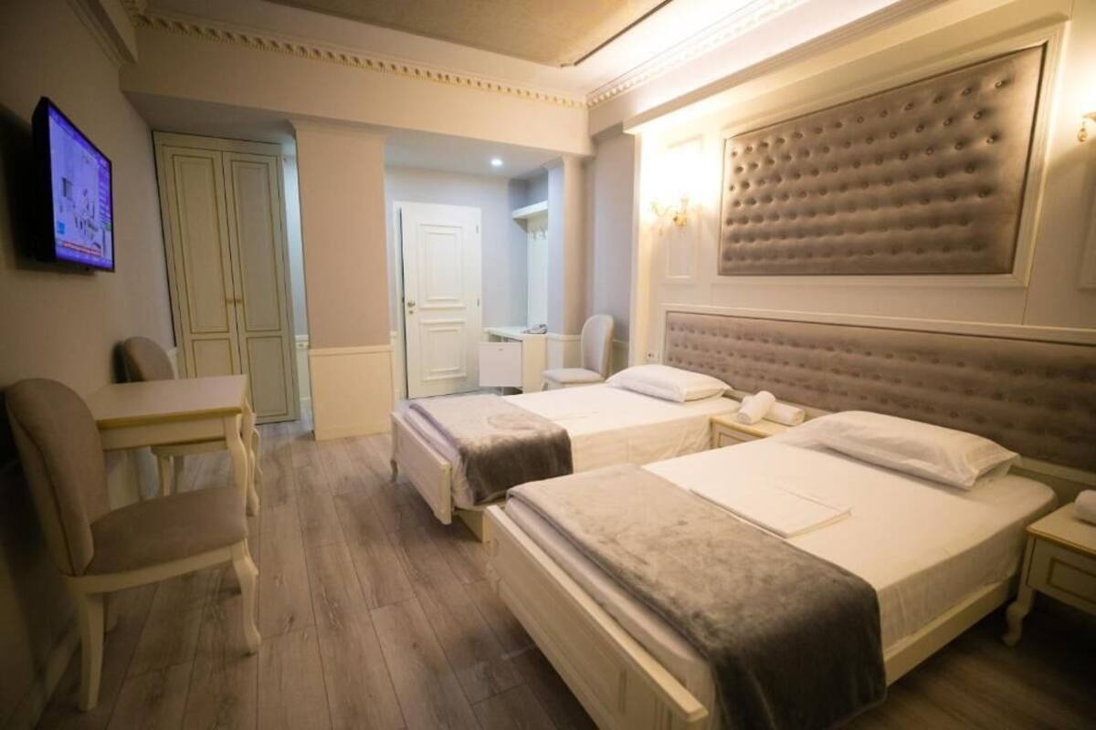A hotel room with two beds, a desk, and a chair. There is a television on the wall and a door leading to another room.
