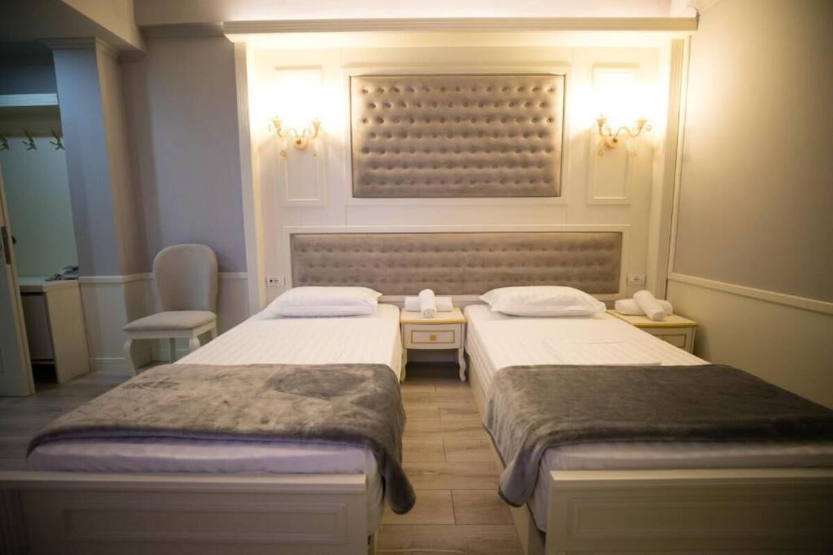 A hotel room with two beds, a headboard with a tufted design, bedside lamps, and a mirror.